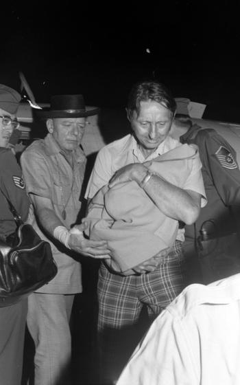 A man holds a child wrapped in a blanket as people around him watch.