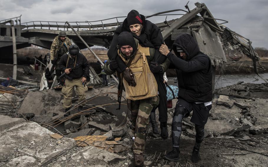 Ukrainian forces carry an elderly man as thousands flee the area of Irpin at a damaged bridge on the outskirts of Kyiv, Ukraine on Monday, March 7, 2022. 