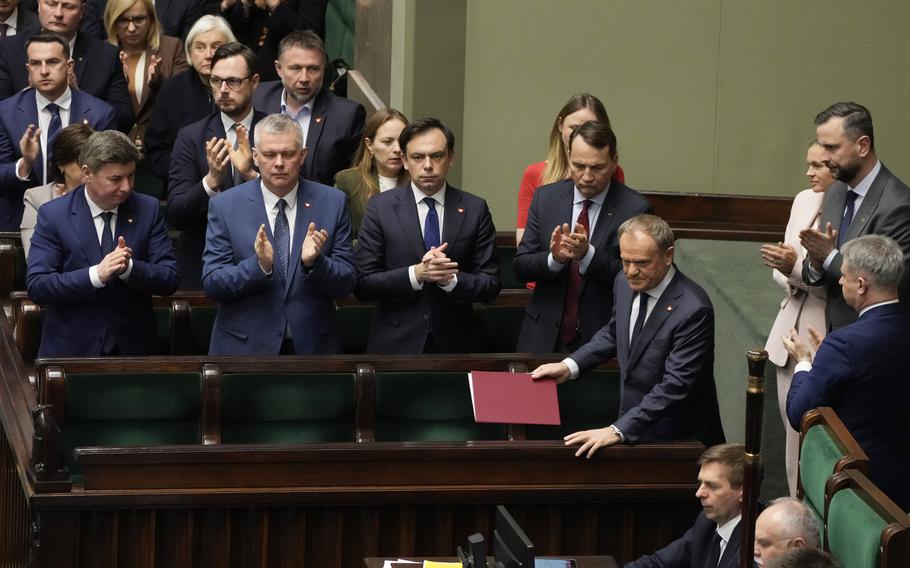 Members of Parliament clap while standing around the Polish prime minister.