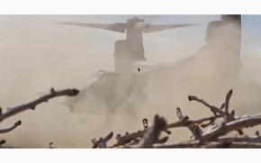 A video screen grab shows an MV-22 Osprey lifting off as it stirs up a cloud of dust.