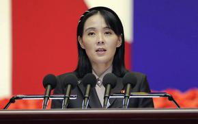 A North Korean woman stands at a podium and speaks into a bank of five microphones.