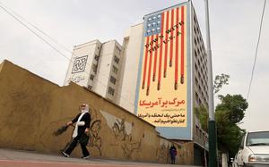 Two women walk on a sidewalk, with a multi-story building looming over them with a mural criticizing the U.S.