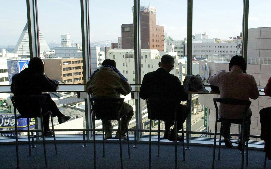 Four men seated in front of an all-glass wall/window that overlooks a cityscape.