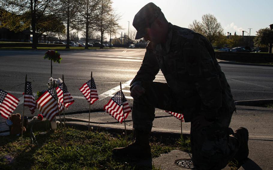 An airman kneels while silhouetted against the sun in the background while paying his respects at a memorial of U.S. flags.
