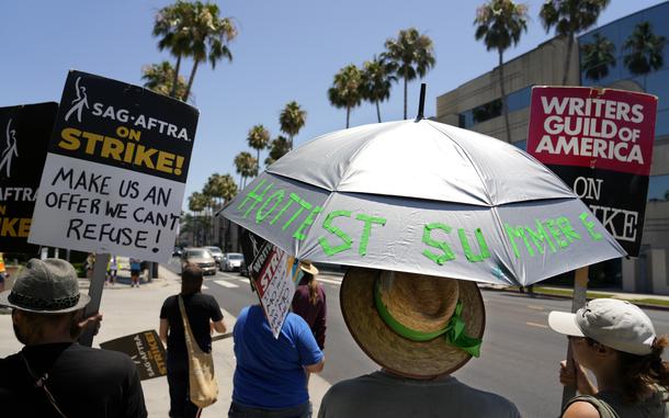 Writers Guild of America captain Mason Flink holds an umbrella to shield himself from the heat as he stands with other picketers in front of Paramount Pictures, Monday, July 24, 2023, in Los Angeles. (AP Photo/Chris Pizzello)