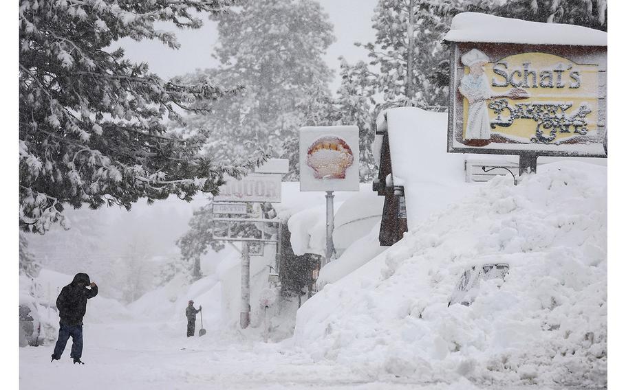 A person walks as snow falls above snowbanks piled up from previous storms during another winter storm in the Sierra Nevada mountains on March 10, 2023, in Mammoth Lakes, California. 