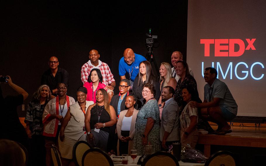 Volunteers and presenters pose for a photo in front of a Tedx screen.