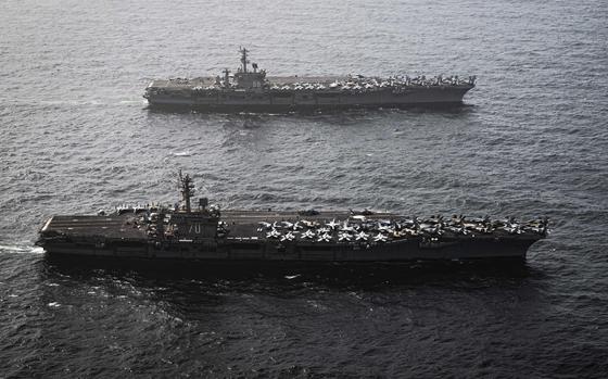 Two aircraft carriers, seen from above, sail side-by-side in open water.