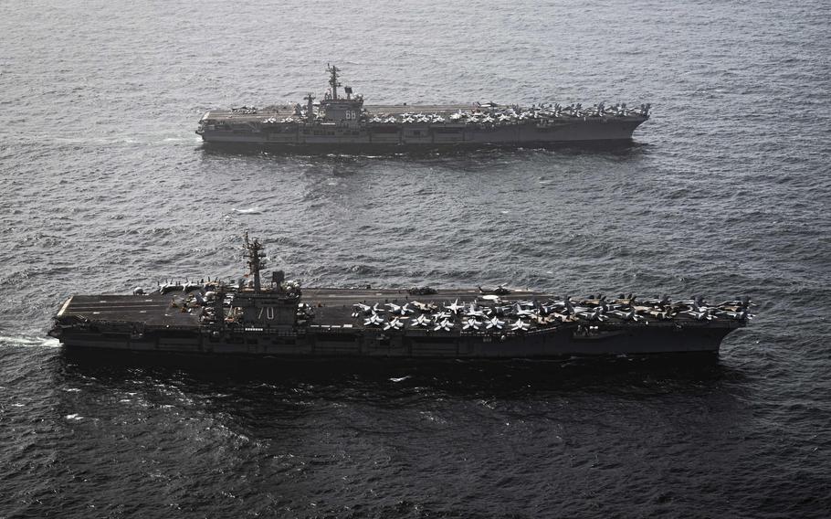 Two aircraft carriers, seen from above, sail side-by-side in open water.