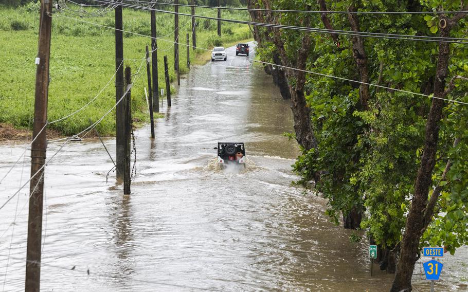 Vehicles drive down a flooded road.
