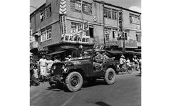 [PUBLISHED CAPTION: Sgt. James D. Rancourt (driving) makes his daily patrol through the streets of Pusan [sic]. 9/8/1957]; Sergeant James D. Rancourt drives his military police jeep through the busy streets of Busan, South Korea, patrolling the area with his Republic of Korea police counterparts. Seated next to him is ROK Sgt. Ha Kung Jin. In the back sits ROK National Police Sgt. Kim Yung Han. The area of U.S. police responsibility in the southern part of the Republic of Korea totals approximately 35,000 square miles. The major activities located within the general area of the city of Busan are the Busan Area Command Headquarters, F Detachment, K MAG, Busan port, the 142nd Quartermaster Battalion, the United Nations Cemetery Compound, K-9 AB; the U.S. Coast Guard station and the German Red Cross hospital. The Provost Marshal Secretary of PAC includes one officer and 95 enlisted men, and they are assisted by a detachment from the 2nd Military Police Det.  (Criminal Investigations, C.I.) for investigation of criminal offenses. [cg]