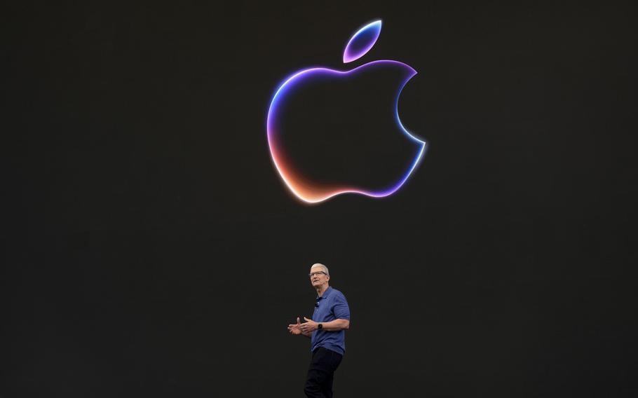 Tim Cook walks underneath an Apple logo against a black background.