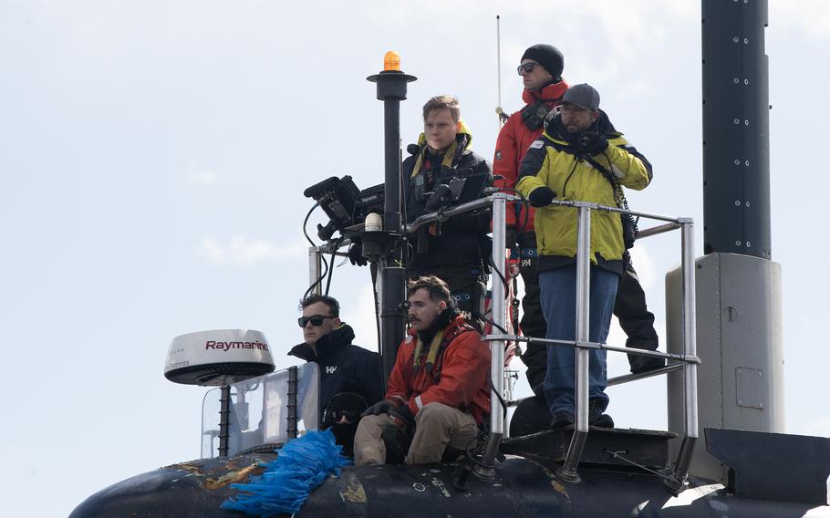 Sailors ride atop the submarine as it prepares to moor.