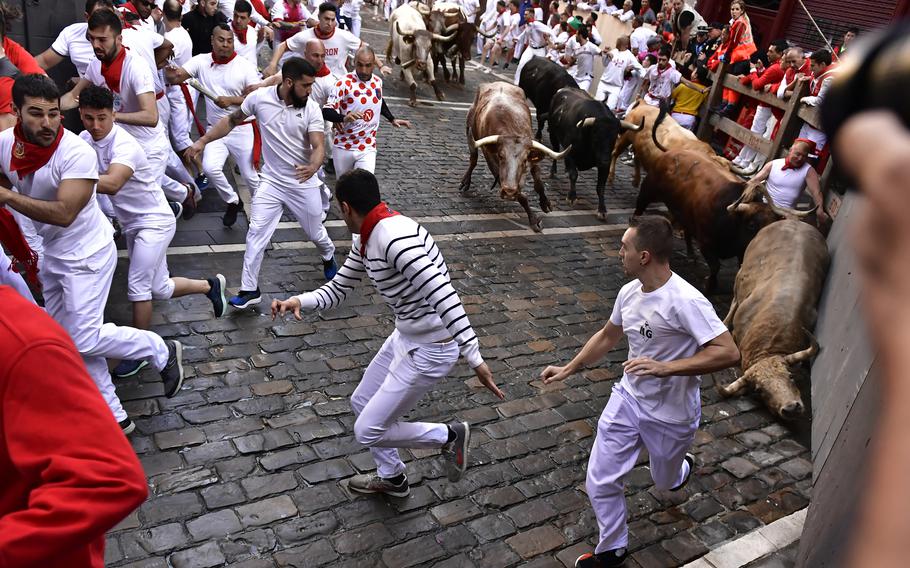 People run through the streets with fighting bulls and steers during the first day of the running of the bulls at the San Fermin Festival in Pamplona, northern Spain, Thursday, July 7, 2022. 