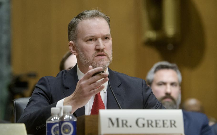 Greer raises his hand and speaks during a hearing. 