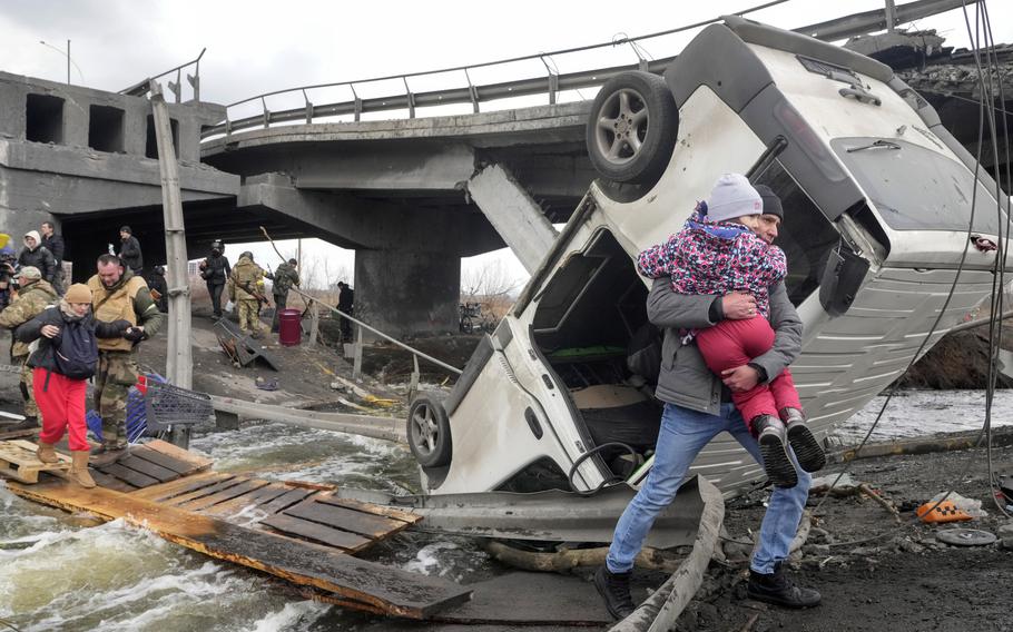 People cross an improvised path under a destroyed bridge while fleeing the town of Irpin close to Kyiv, Ukraine, Monday, March 7, 2022. 
