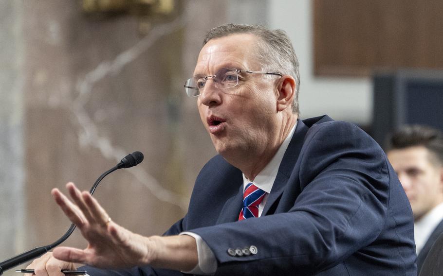 Collins seated, raising his left hand and speaking into a microphone.
