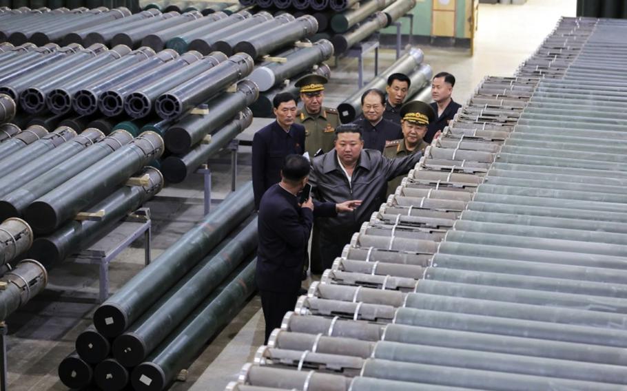 Kim Jong Un, with an entourage of men in suits and military uniforms, inspects a Pyongyang weapons factory.