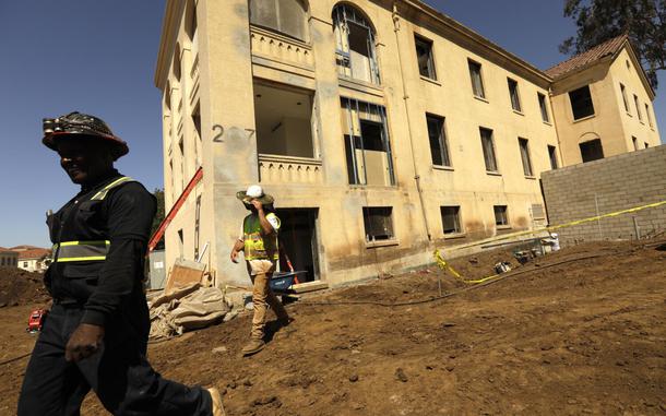 LOS ANGELES, CA - JUNE 23, 2022 - - Construction workers walk past Building 207 that is being refurbished as housing for veterans on the Veteran Affairs West LA campus in Los Angeles on June 23, 2022. This is the Collective's first project, a 60-unit building for senior veterans and their families and is scheduled to open this fall. Along with U.S. VETS, the Collective is made up of Century Housing, a nonprofit that builds and finances affordable housing, and Thomas Saffran and Associates, a Brentwood-based for-profit affordable housing developer. The master plan calls for 14 buildings to be brought up to current standards but preserved in their original form with another 14 built from the ground up. (Genaro Molina / Los Angeles Times)