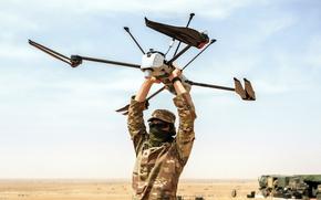 A solider holds a drone over her head in a desert setting.