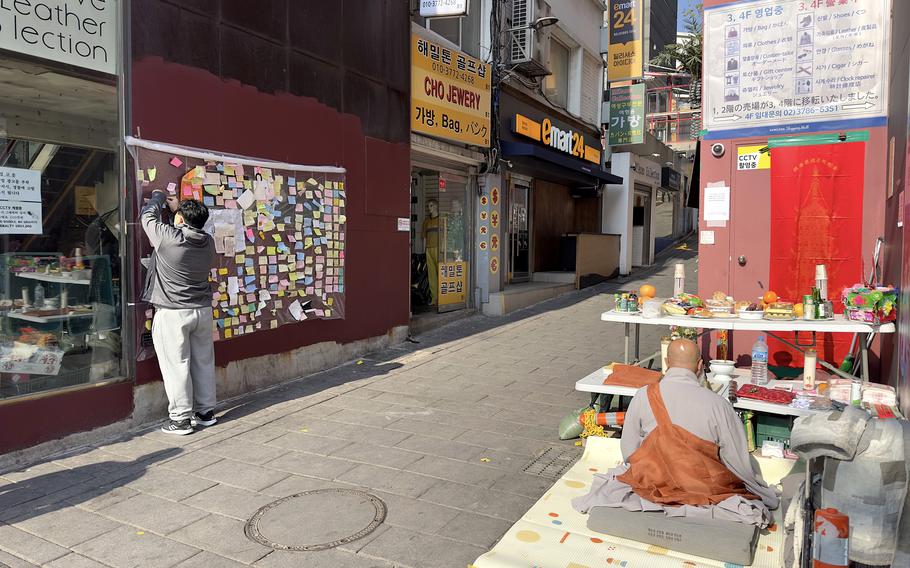 A man places a written tribute as a Buddhist monk prays at an alleyway where a crowd surge killed at least 158 people last month in Itaewon, South Korea, Nov. 17, 2022.