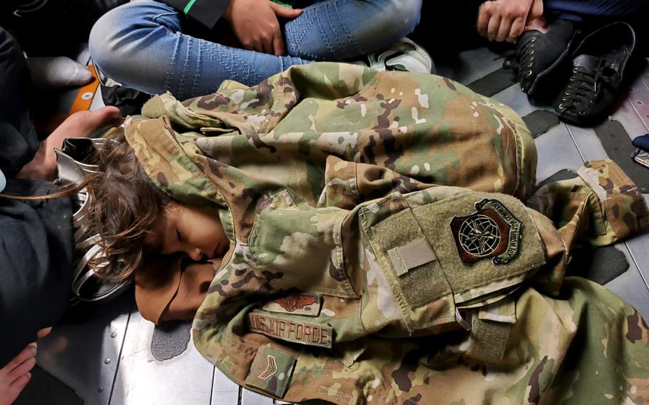 An Afghan child sleeps on the cargo floor of a U.S. Air Force C-17 Globemaster III, kept warm by the uniform of the C-17 loadmaster, during an evacuation flight from Kabul, Afghanistan, Aug. 15, 2021.