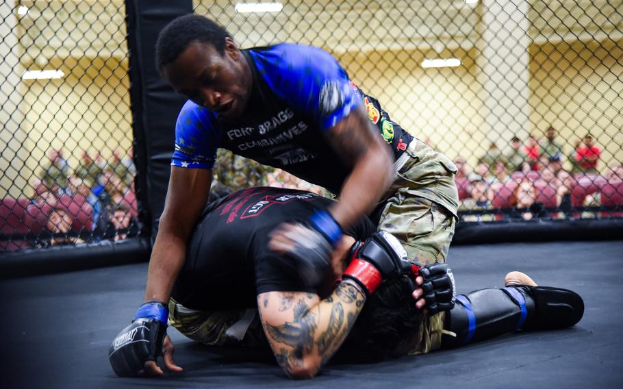 A partly blurry photo of two fighters in a cage, one curled over protecting his head while the other kneels above him.