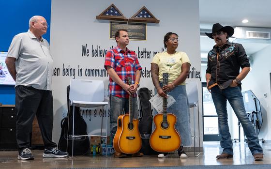 Singer and songwriter Carl Wayne Meekins, right, shares his story and how that compelled him to start his Play it Forward Campaign as recent graduates of Guitars 4 Vets, Jacob Scissions, second left, and Ariel Jarvis, second right, listen during a Guitars 4 Vets guitar donation hosted by Every Third Saturday in Minneapolis on Monday, June 23, 2025. The ceremony celebrated veterans who had completed 10 weeks of guitar lessons through Guitars for Vets, a national organization that provides free guitars and music lessons to veterans. Mark Shirk, Minneapolis Guitars for Vets chapter coordinator, stands to the left. (Bennett Moger / Pioneer Press)