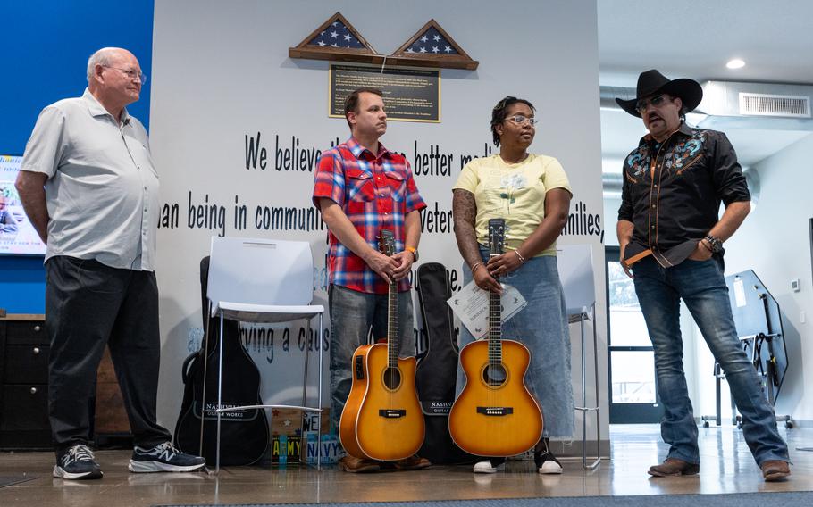 Four people standing, two holding acoustic guitars