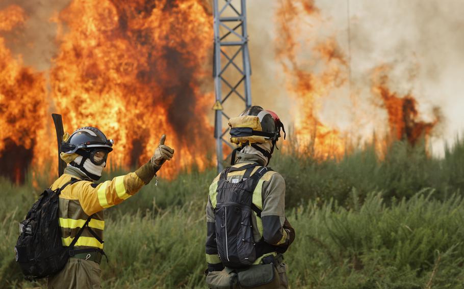 Firefighers in helmets and protective gear face a blaze.