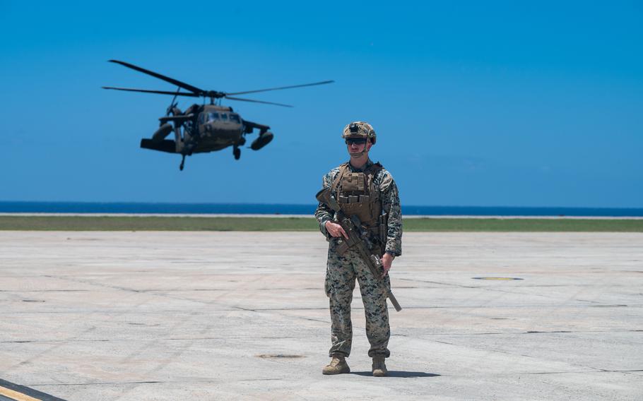 Marines stands on a tarmac with a helicopter flying behind him.