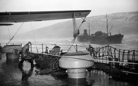 The crew of a seaplane tender struggles to secure seaplanes during a storm off the coast of Hvalfjordur, Iceland, in 1941.