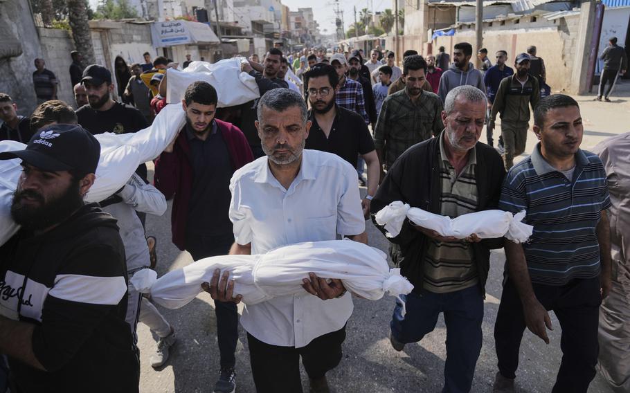 A group of Palestinian men walk down a street in Gaza carrying the white shroud-covered bodies of relatives killed in an airstrike.