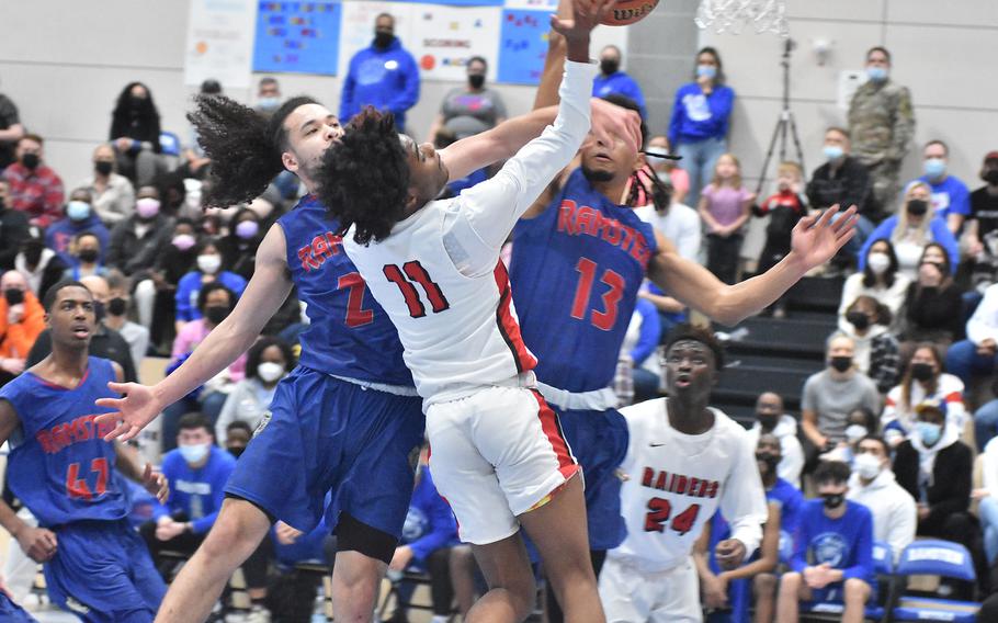 Kaiserslautern’s Kevan Williams collides with Ramstein’s Israel Rouse, left, and Ezra Woodfork while trying to score in the DODEA-Europe Division I boys basketball title game on Saturday, Feb. 26, 2022.