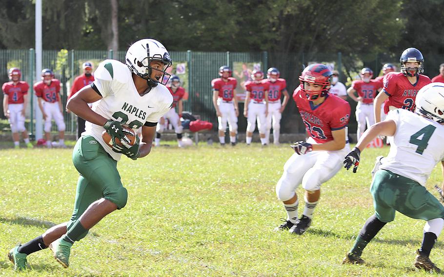 Naples’ Keshawn Holland takes a handoff and tries to go past Aviano Saints defenders during Saturday’s football game held at Aviano. The Wildcats won the game decisively by the score of 40-0. 