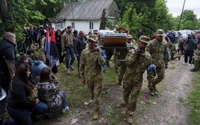 Ukrainian service members carry a coffin along a dirt path.
