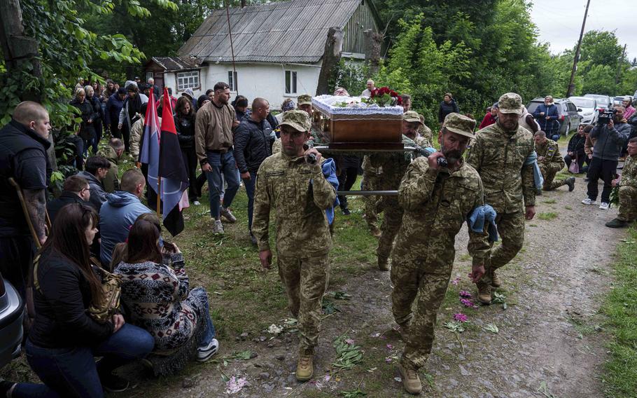 Ukrainian service members carry a coffin along a dirt path.