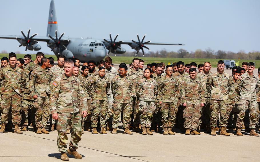 Soldiers stand in formation with an aircraft in the background
