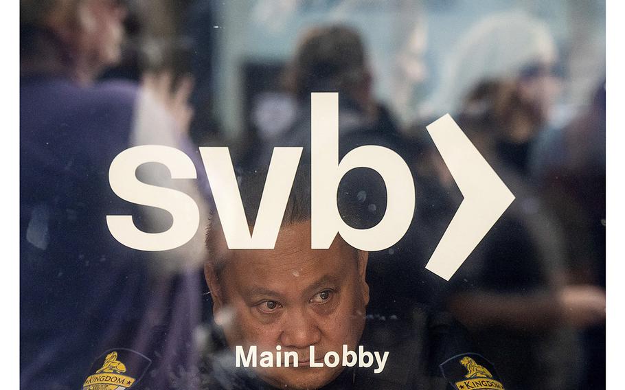 A security guard looks out a door as customers line up at Silicon Valley Bank headquarters in Santa Clara, California, on March 13, 2023. 