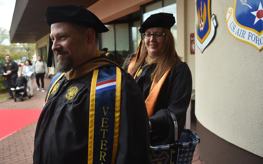 Erin Narvaez, an Air Force spouse, adjusts the hood worn by master’s degree graduate Army veteran Bryce Williams at the University of Maryland Global Campus Europe spring commencement on Saturday, April 27, 2024, at Ramstein Air Base, Germany. Williams, who served 24 years in the Army, said he lost track of how many years it took him to earn his bachelor’s before his master’s degree. “I was doing one class at a time, so it took me a long time,” he said.