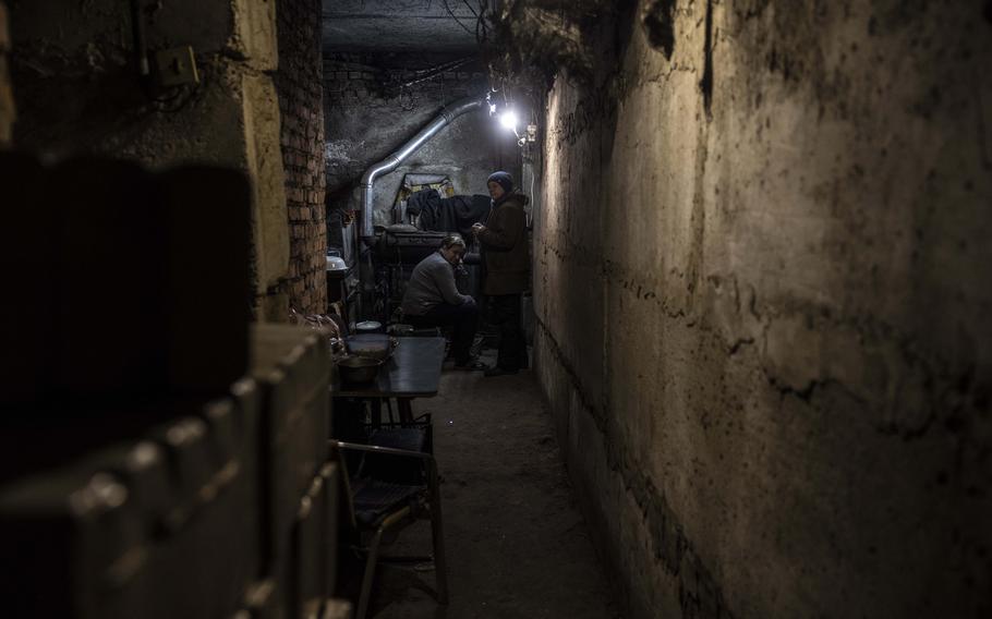 Zoya Konstantinovna, 67, sits near a wood-burning stove with her neighbor in the basement of their apartment building in Lyman on Dec. 17.