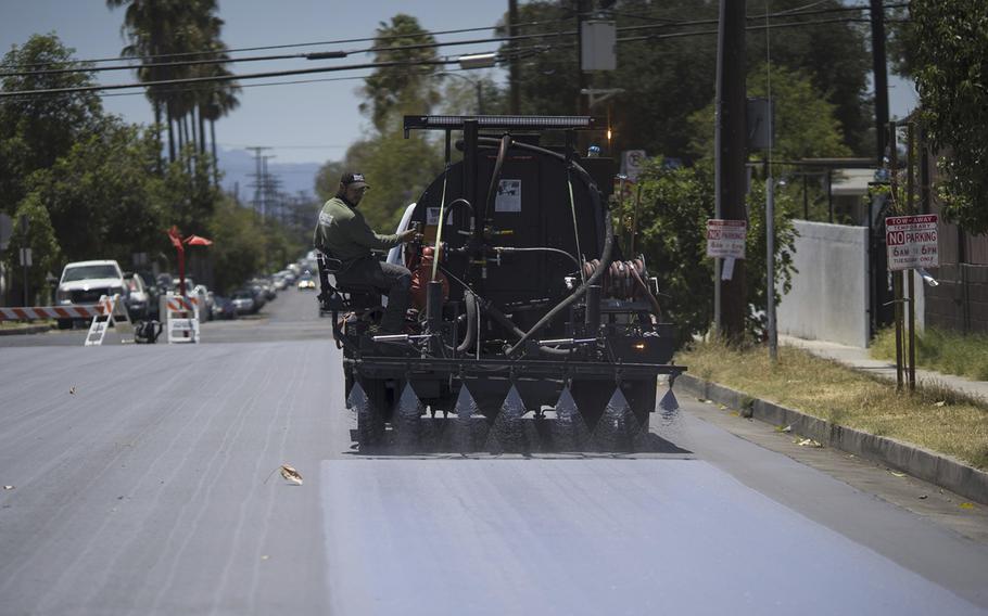 A worker applies a reflective coating to a street in Pacoima, Calif., on July 19, 2022.