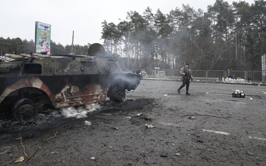 A volunteer of Ukraine’s Territorial Defense Forces walks by a damaged armored vehicle at a checkpoint in Brovary, outside Kyiv, Ukraine, on Tuesday, March 1, 2022. Russian shelling pounded civilian targets in Ukraine’s second-largest city Tuesday and a 40-mile convoy of tanks and other vehicles threatened the capital — tactics Ukraine’s embattled president said were designed to force him into concessions in Europe’s largest ground war in generations.