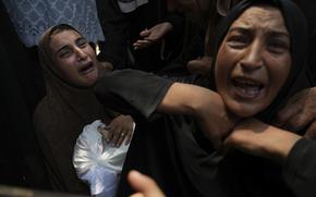 Women wail as they hold a cloth-covered body.