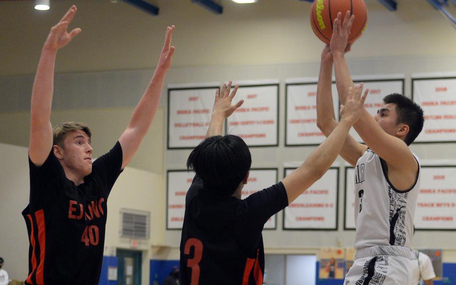 Zama‘s Joshua Caburian shoots over E.J. King’s Arjae Laurente and Jacob Auger during Thursday’s DODEA-Japan boys basketball tournament game. The Trojans won 65-56.