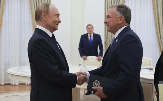 Vladimir Putin shakes hands with Steve Witkoff in a white room, both smiling.