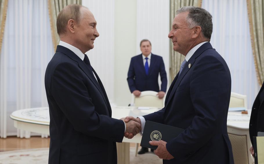 Vladimir Putin shakes hands with Steve Witkoff in a white room, both smiling.