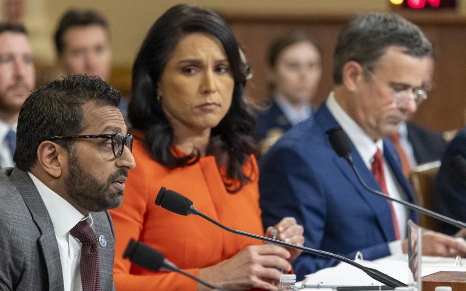 Patel speaks into a microphone as Gabbard looks on and Ratcliffe looks down.