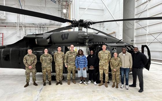 Airmen and football players pose for a picture in front of a Blackhawk helicopter