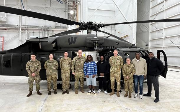 Airmen and football players pose for a picture in front of a Blackhawk helicopter